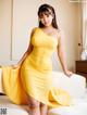 A woman in a yellow dress posing on a white couch.