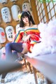 A woman in a kimono sitting on a chair in front of lanterns.