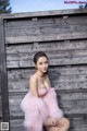 A woman in a pink dress sitting on a wooden fence.